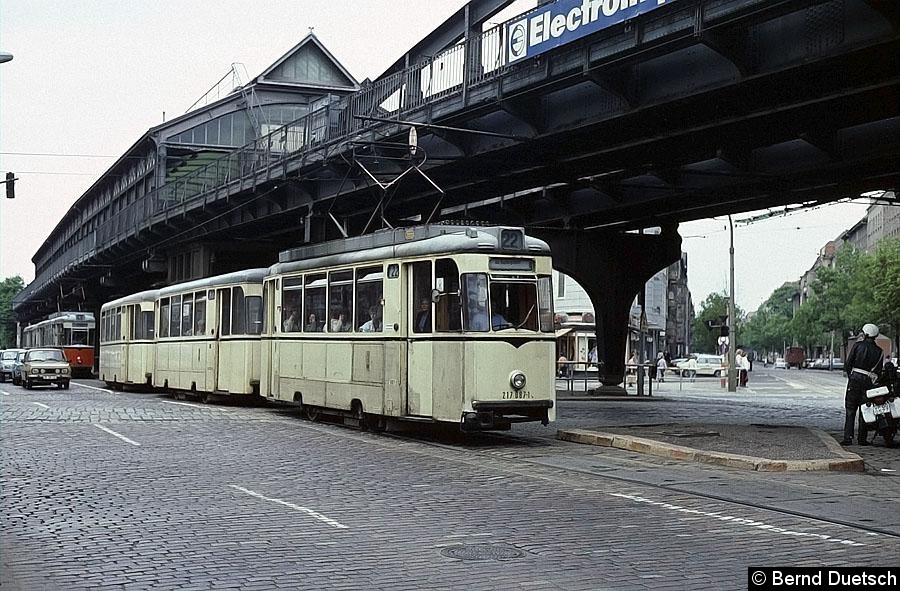Bild: Unter dem Viadukt der U-Bahn-Linie 2 in der Schönhauser Allee fährt ein Dreiwagenzug der Linie 22 Richtung Innenstadt. 
Ihm folgt ein Dreiwagenzug der Linie 49. Die querenden Gleise wurden damals von der Linie 4 befahren. Anscheinend interessiert sich der im Bild rechts zu sehende VOPO ebenfalls für die Straßenbahn.